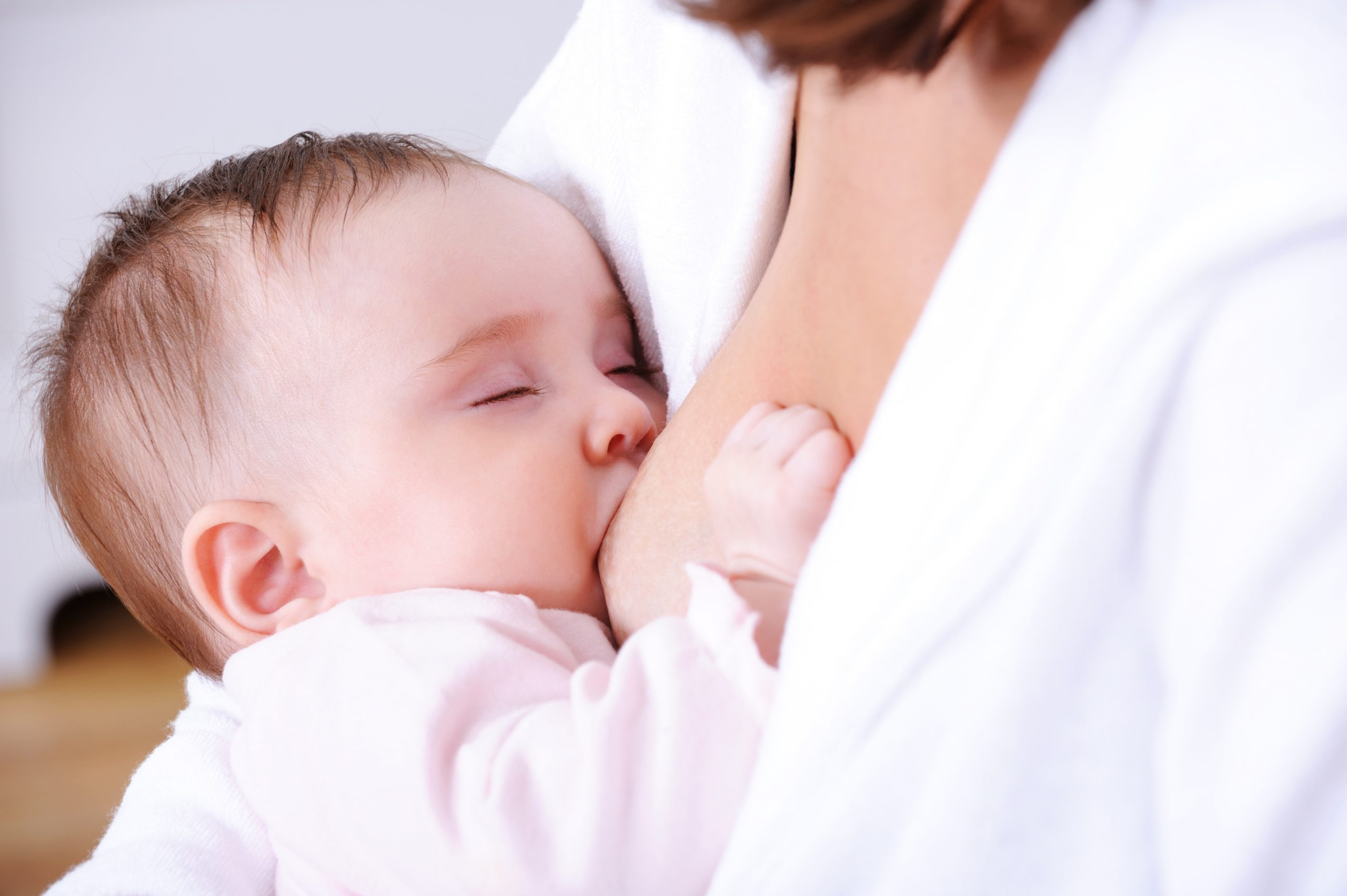 Breastfeeding for little beautiful newborn baby with closed eyes - indoors